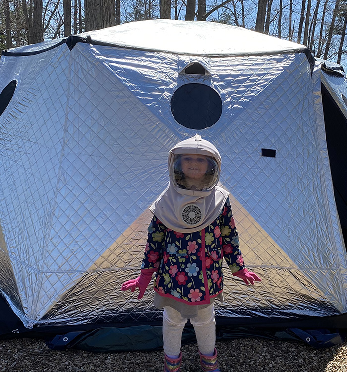 girl in front of tent wearing protective hat with face shield and fan