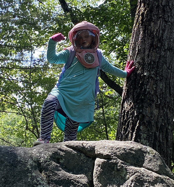 girl standing on rock beside a tree wearing protective hat with face shield and fan