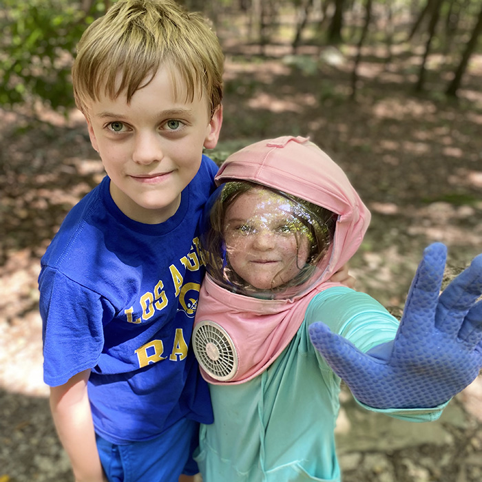 boy and girl standing outside. girl wearing protective hat with face shield and fan