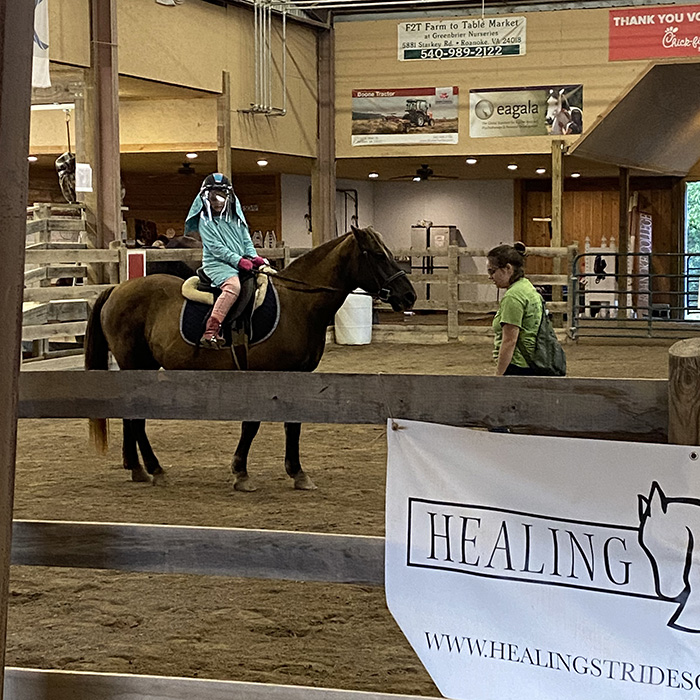 girl in protective clothing riding a horse in indoor horse ring