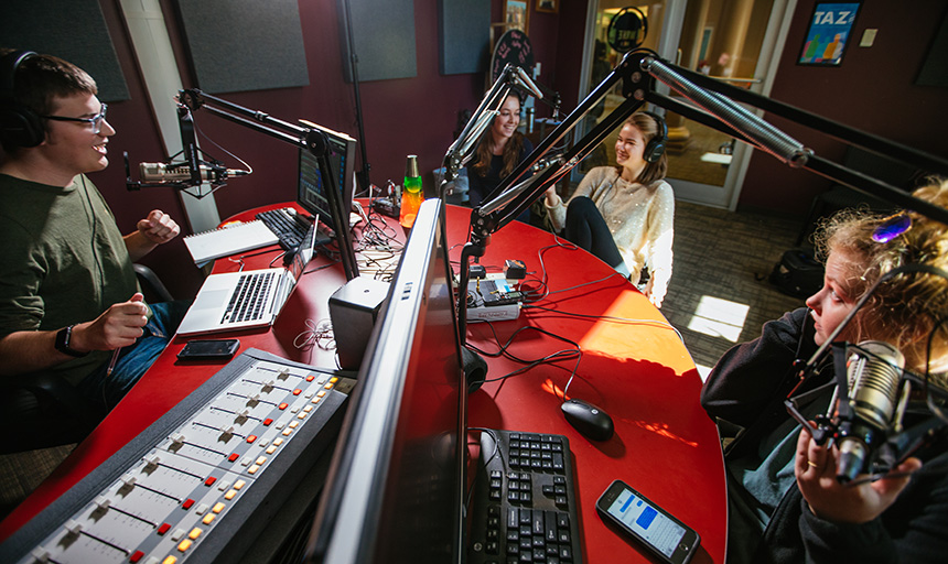 Several students talking in radio station with equipment around them