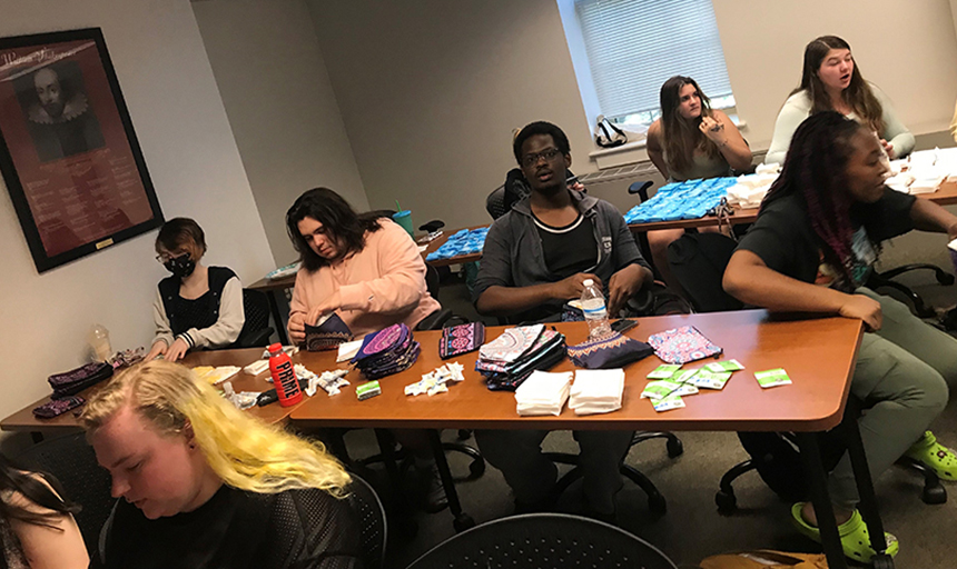 Seven students sit at tables and organize materials for packaging