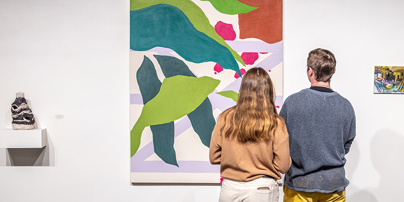 A woman and a man gaze at a large painting featuring green, leaf-life imagery