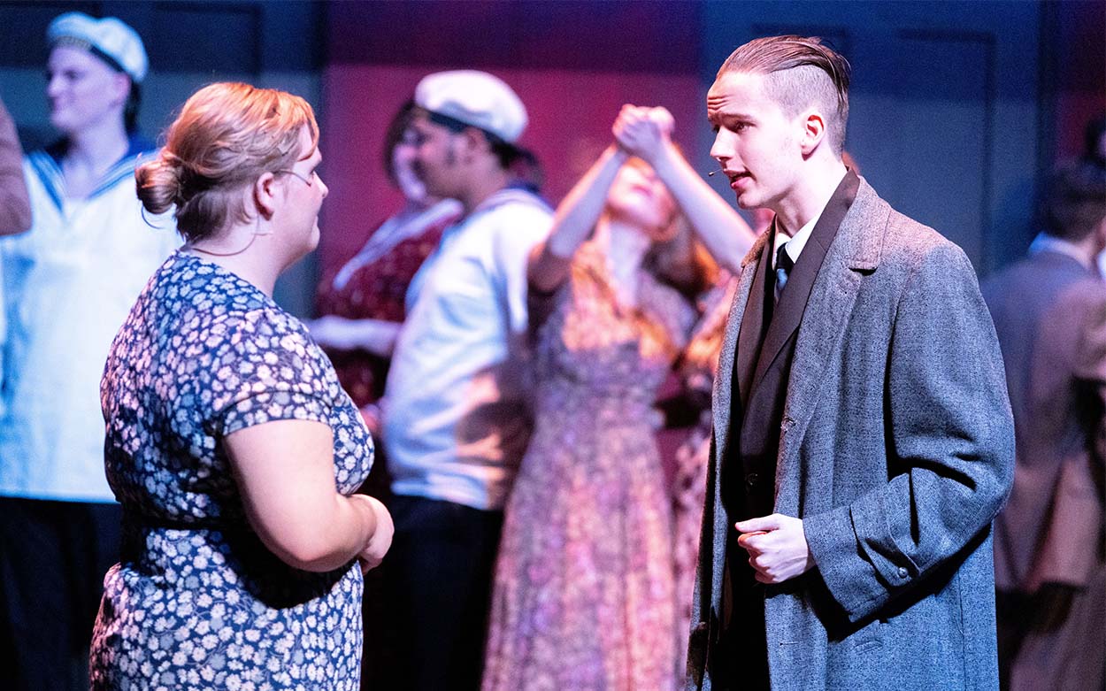 A man and woman talking with dancers in the background.