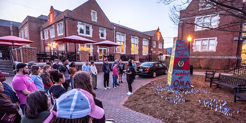 Vigil attendees gather around The Rock, an obelisk structure on campus, after surrounding it with small stakes planted in the ground that bear the names of enslaved people