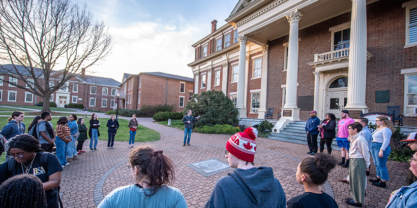 Students and faculty gather in a circle around the campus seal while listening to information about the history of the construction of the adjacent administration building
