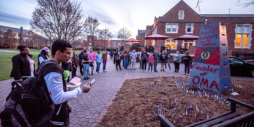 Vigil attendees gather around The Rock, an obelisk structure on campus, after surrounding it with small stakes planted in the ground that bear the names of enslaved people