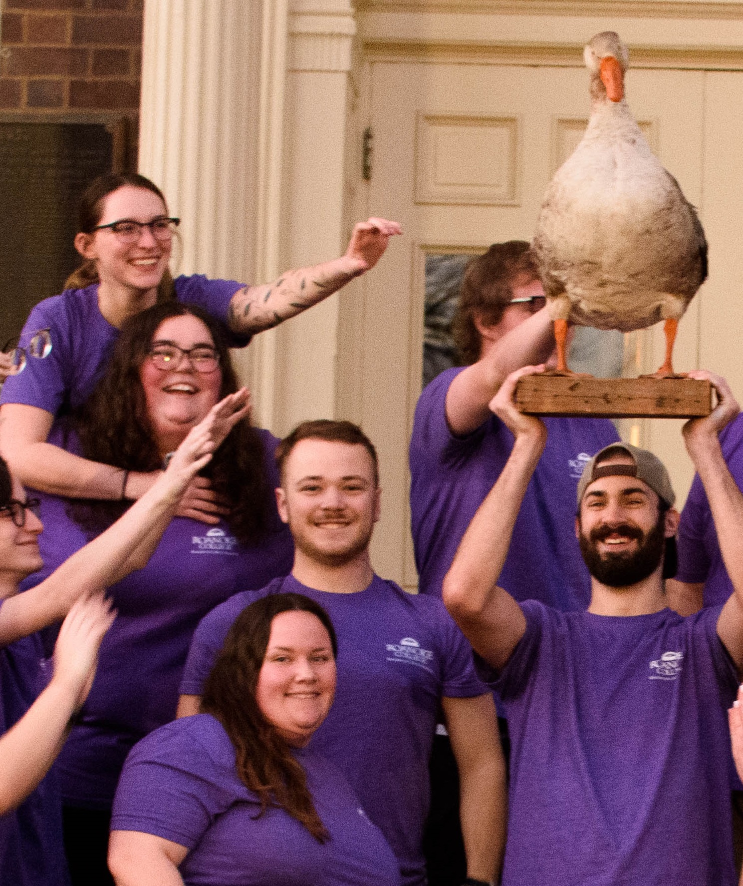 Resident advisors laugh as one holds a stuffed goose up over his head in a triumphant gesture