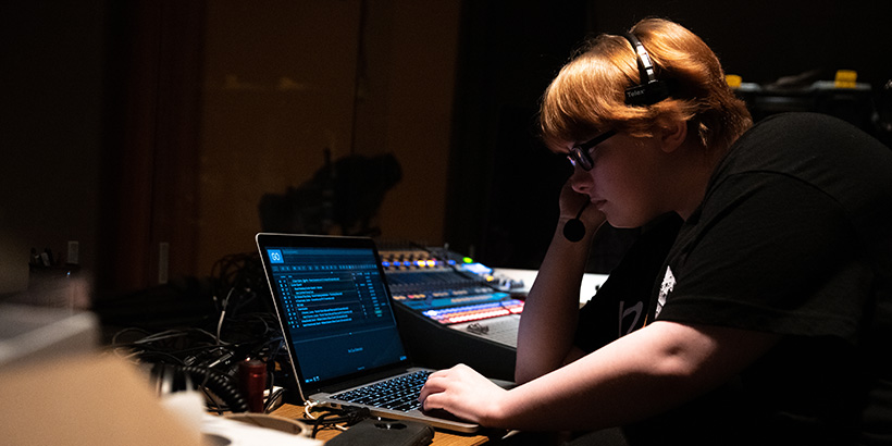 A backstage crew member monitors a computer while listening to others through a headset
