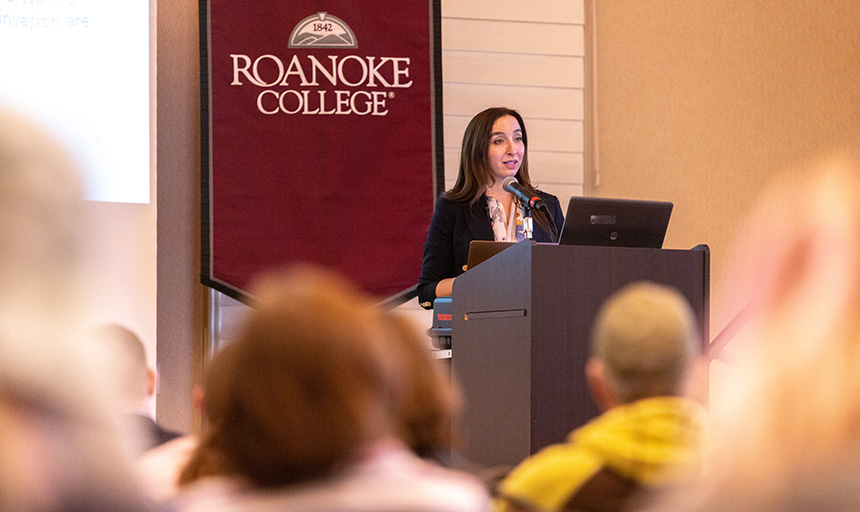 Leila Hanafi speaks from the dais in the Wortmann Ballroom with a Roanoke College banner draped in the background