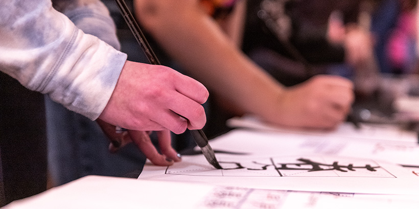 A closeup image of a paintbrush gliding across a piece of paper at the calligraphy station set up for the Lunar New Year celebration