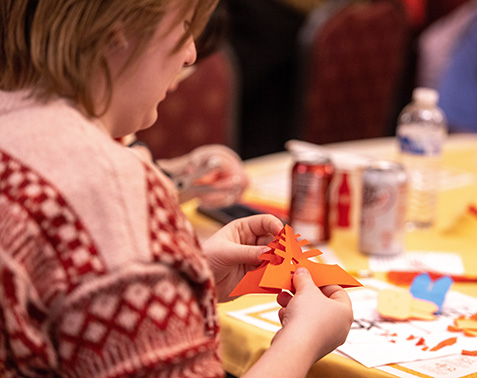 A student sitting at a table folds a piece of paper to create an origami figure