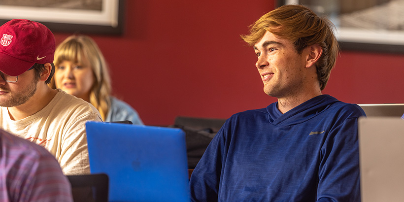 A student with a laptop opened on his desk smiles during a discussion