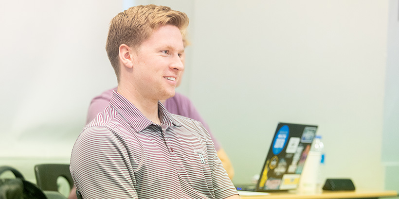 A student seated at a desk smiles during a class discussion