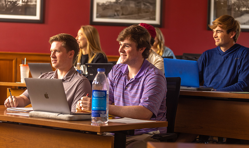 Students sitting in a classroom of tiered desks smile during a discussion