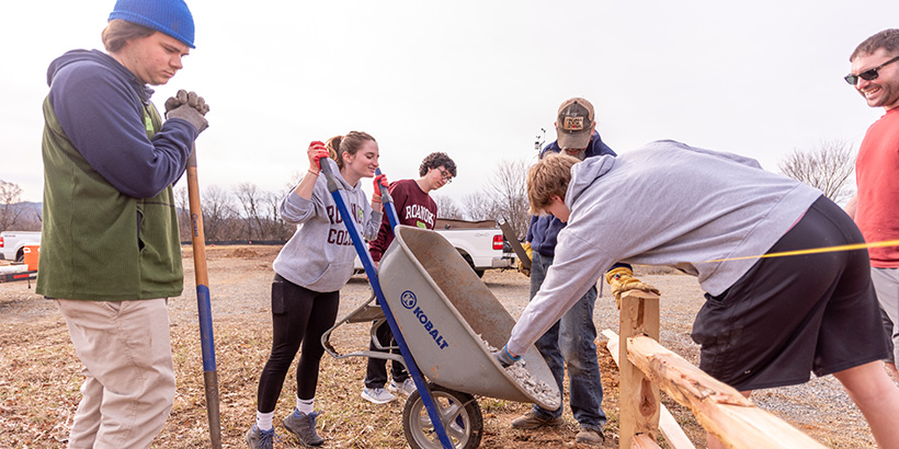 Students carry shovels and dump gravel from a wheel barrow