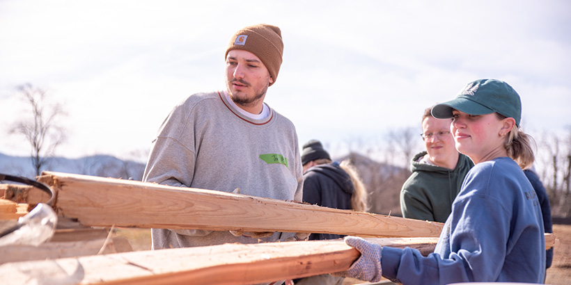 Two students carry a wooden fence plank