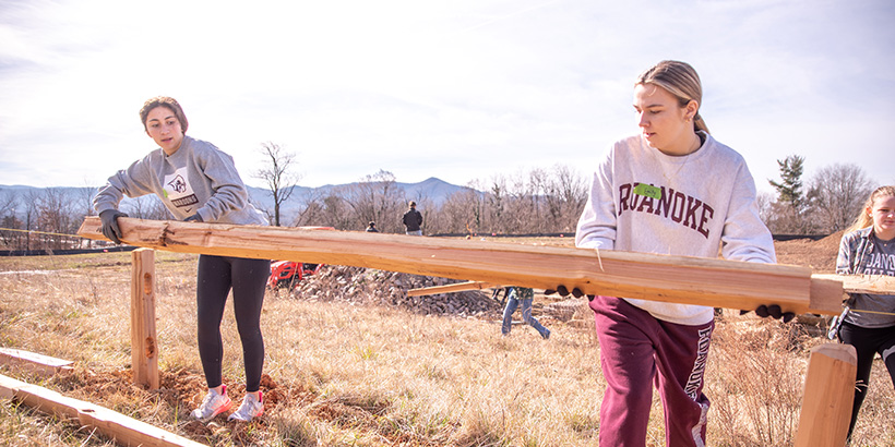 Two student put a wooden plank in place along a new fence being built