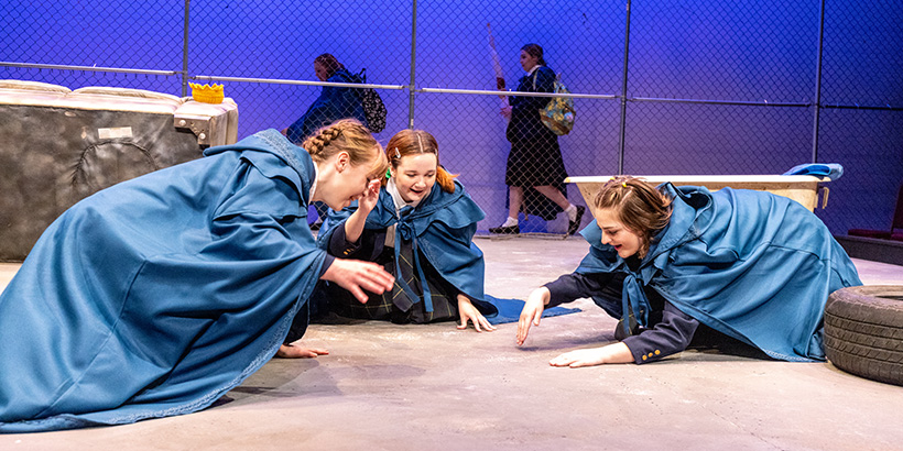 Actors playing the Three Witches of Macbeth kneel on the floor in a circle