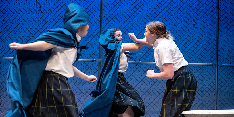 Two actors attack another actor. swinging their arms toward her, in a fight scene