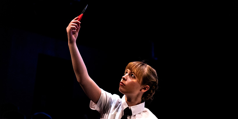 An actor holds a blade in the air and gazes at it with an ominous expression