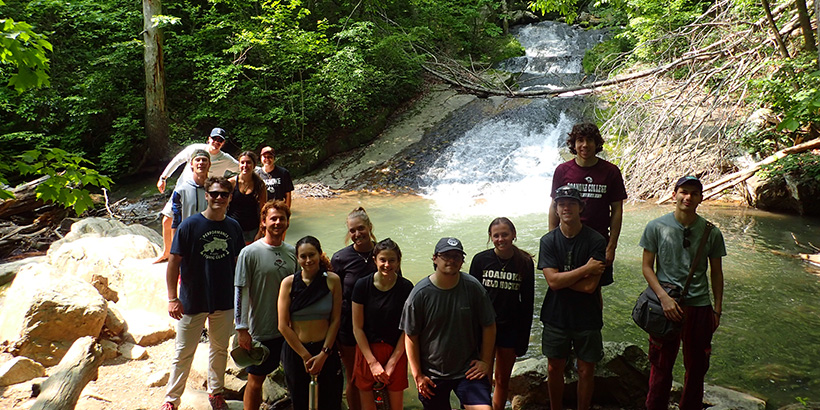 Students stand along the rocks that overlook a pool of water at the bottom of a waterfall