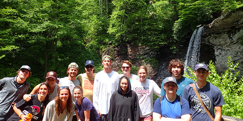Students lean in and smile for a photo against the backdrop of a waterfall