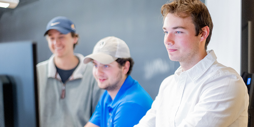 Three students gather around a computer screen as their experiment results start coming in