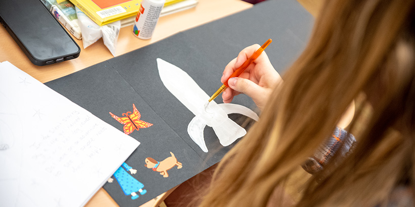 A student paints an illustration of a rocket ship for her Science Storytelling project