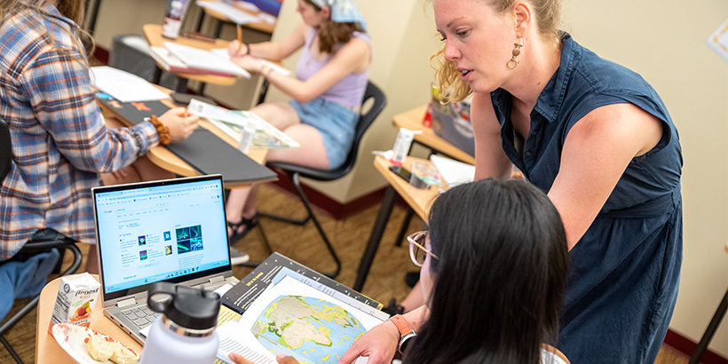 A teacher leans down to examine a book while discussing a point with a student 