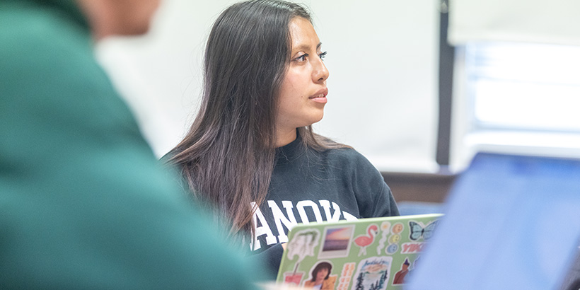 A student with a laptop open in front of her listens during a classroom discussion