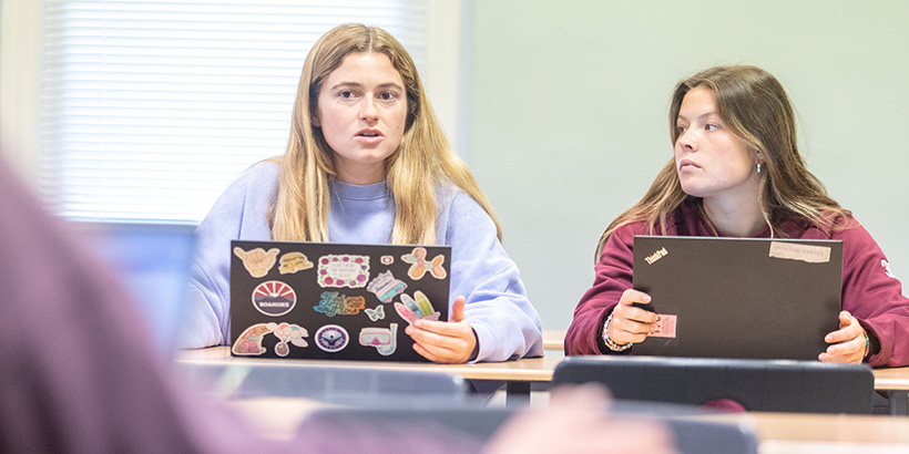 A student with a laptop decorated with stickers speaks during a classroom debate