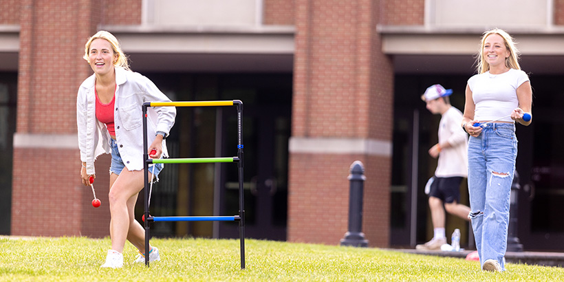 Two smiling students, one about to release a throw, take part in a ladder toss game