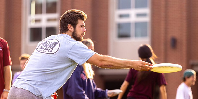 Close-up photo of a student extending his arm to toss a frisbee