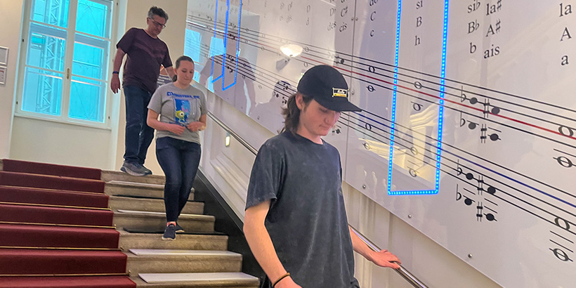 Students walk down a stairwell with a lighted display of musical notes along its wall