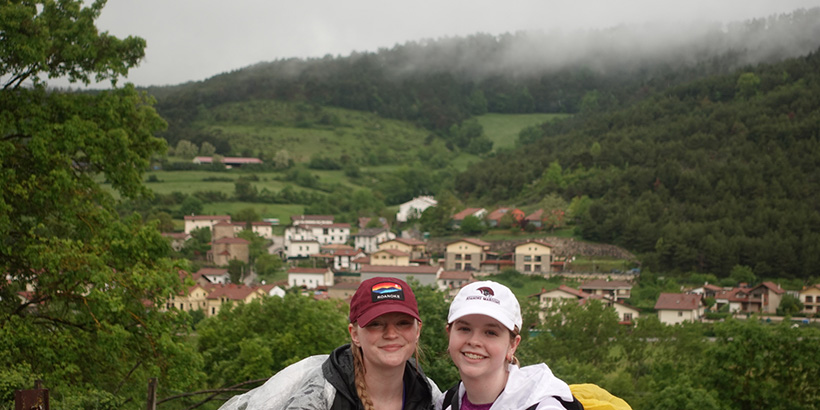 Two students, both wearing different Roanoke ball caps, smile for a photo with a lush, fog-covered valley in the background