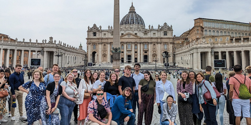 Students smile for a group photo outside a historical building topped by an intricately carved dome