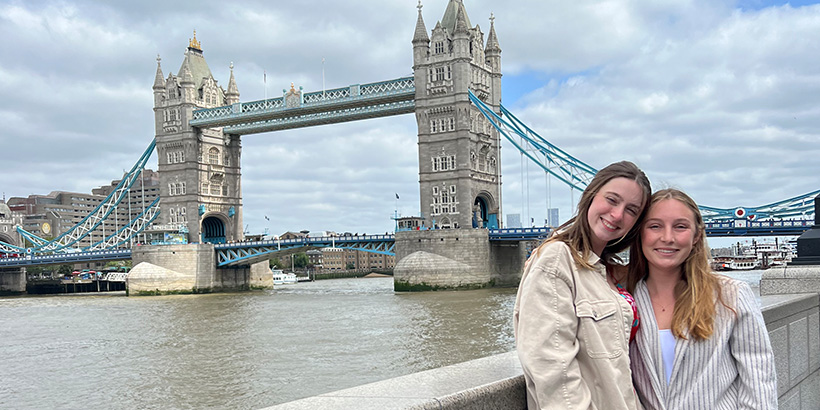 Two students smile for a photo with the London bridge in the background