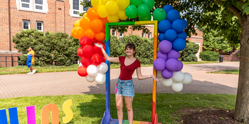 A student shows off a rainbow-hued photo booth station complete with a balloon arch