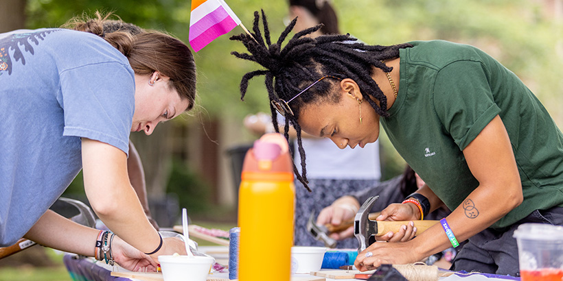 A student wielding a hammer leans forward to work on her project at the string art booth