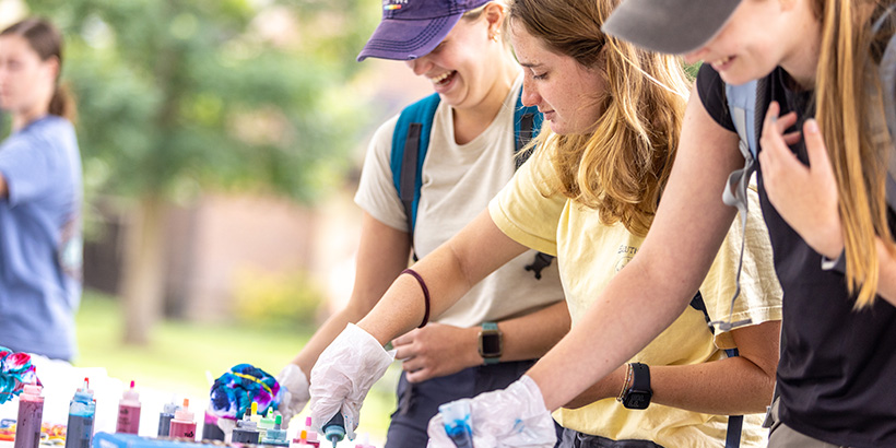 Students wearing protective gloves smile while doing tie-dye projects