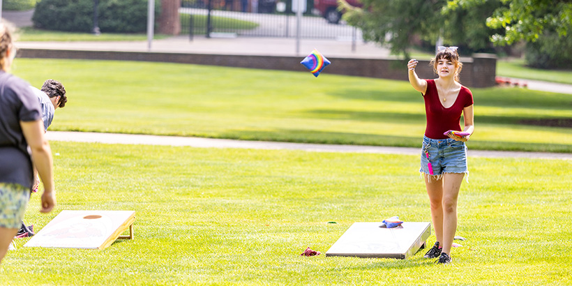 Students play cornhole on the campus quad with beanbags printed with a rainbow design