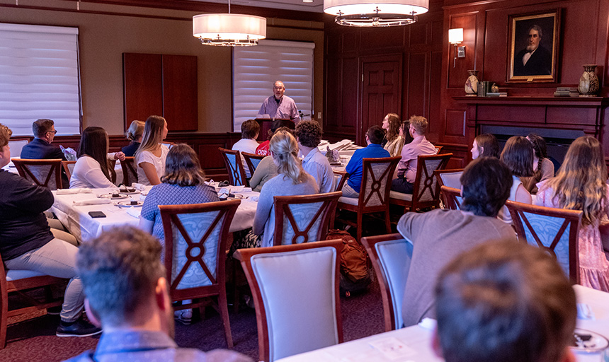 Professor Todd Peppers stands and addresses students who are seated at tables in the President's Dining Room