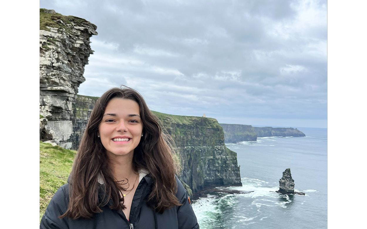 Zoe Pitney smiling with a view of a cliffside overlooking the ocean int