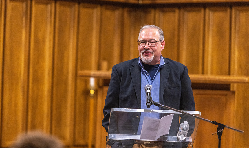 Todd Peppers speaks from a podium inside the wood-paneled sanctuary of Antrim Chapel