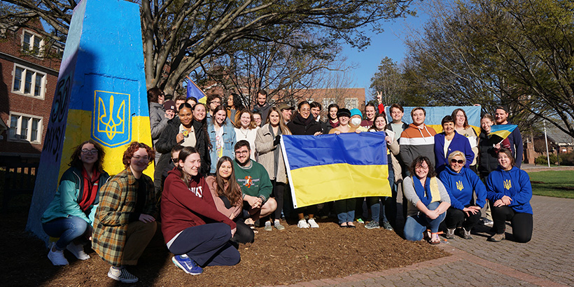 Students and faculty hold Ukraianian flags next to The Rock, an obelisk on the back quad, which is also painted in Ukrainian colors