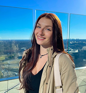 Gabrielle Liorsi smiles for a photo on a outdoor overlook with a view of a bright sky