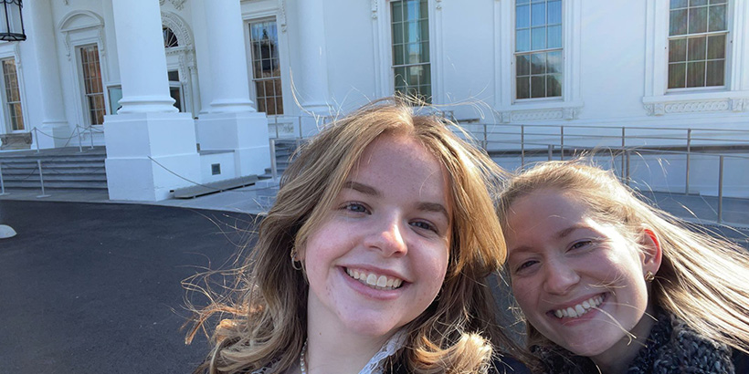 Tori Weed smiles with a friend outside the entryway columns of a D.C. building