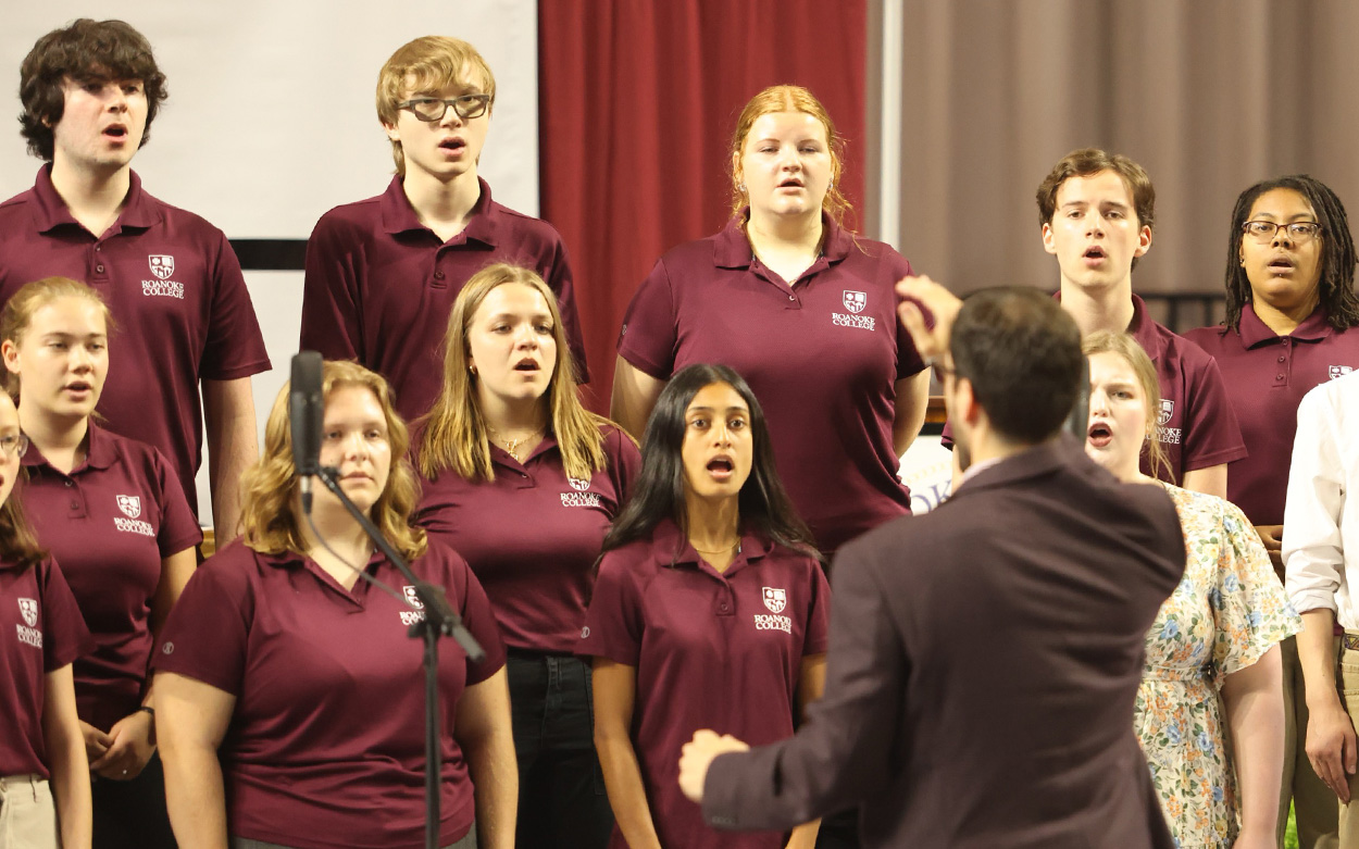 Choir members dressed in matching maroon shirts sing from the stage