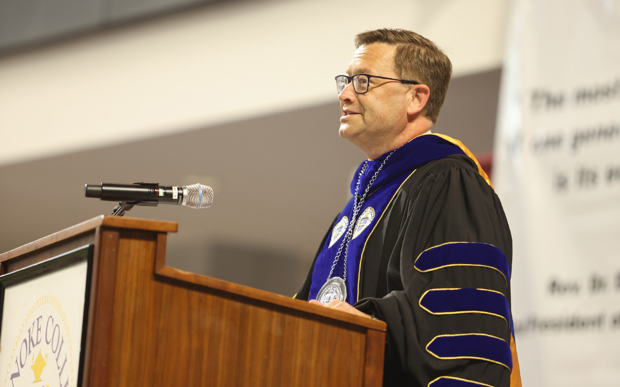 President Shushok, dressed in an academic regalia robe, greets the gathering from a podium
